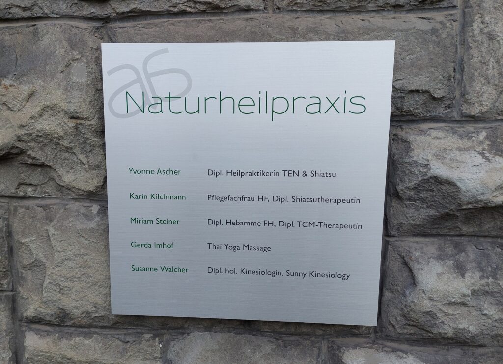 Metallschild mit der Aufschrift ‚Naturheilpraxis‘ und den Namen mehrerer Therapeutinnen.